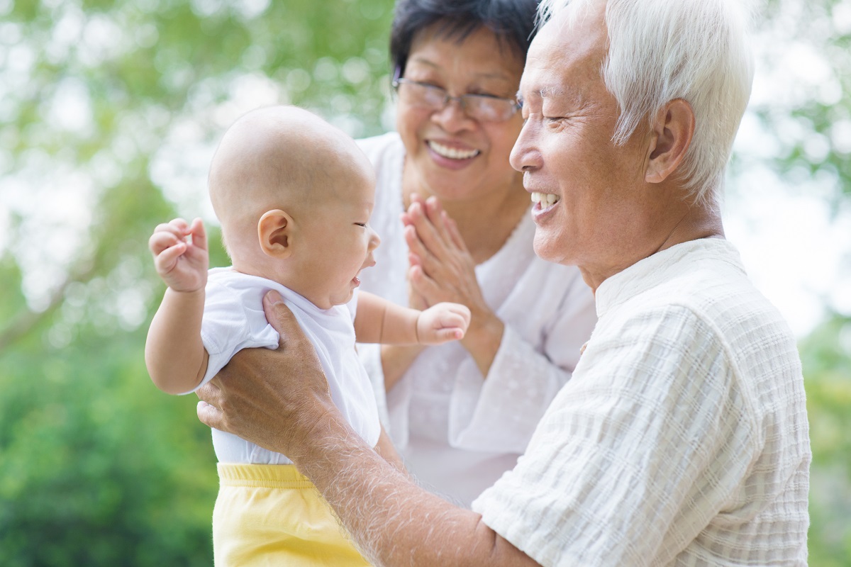 Happy Asian grandparents playing with baby grandchild at outdoor garden.